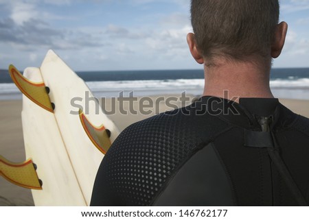 Rear view closeup of male surfer with surfboard on beach looking at sea