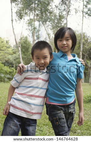 Portrait of happy brother and sister standing arms around in park