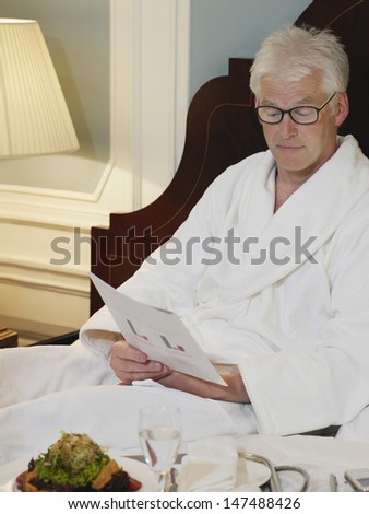 Middle aged man in bathrobe reading document in bed