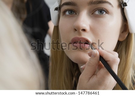 Closeup of a hand applying lipstick to female model\'s lips