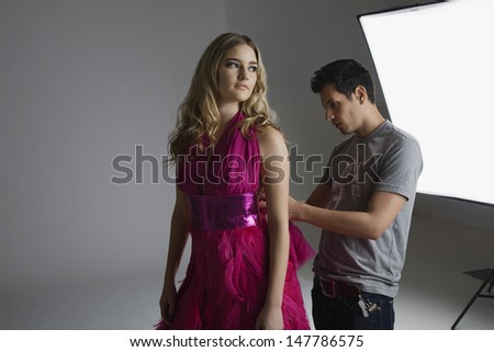 Male designer adjusting dress on a fashion model in studio