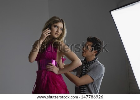 Male designer adjusting dress on a fashion model while she\'s on call in studio