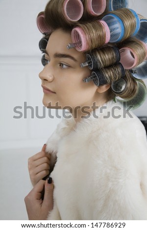 Closeup side view of a female model in hair curlers and fur coat