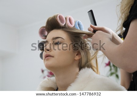 Closeup low angle view of a cropped stylist fixing rollers in female model\'s hair