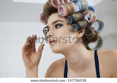 Closeup of a beautiful model in hair curlers using eyelash curler