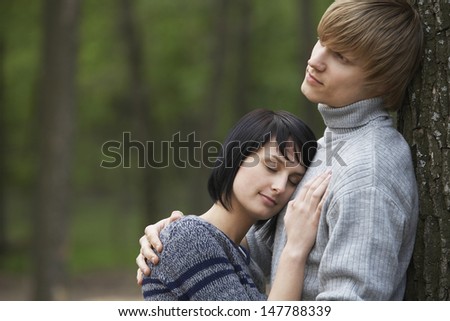 Side view of a young woman laying head on man\'s chest in woods