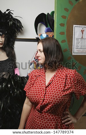 Thoughtful female owner standing by costumes at the second hand store