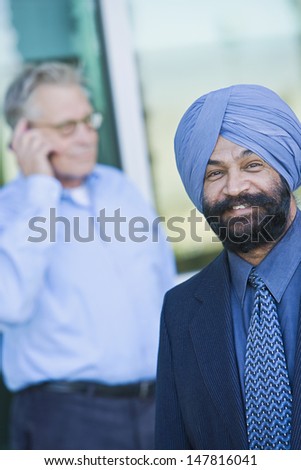 Portrait of a smiling Indian businessman with colleague using cellphone in background