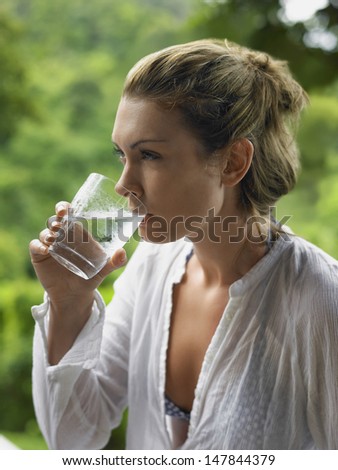 Closeup side view of a young woman drinking water against blurred plants