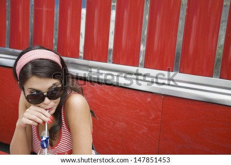 Closeup of a young woman in sunglasses drinking soda