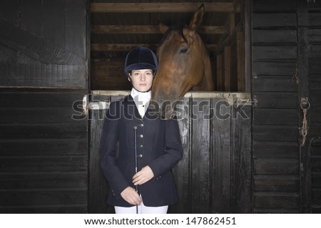 Portrait of a confident female horseback rider with horse in the stable