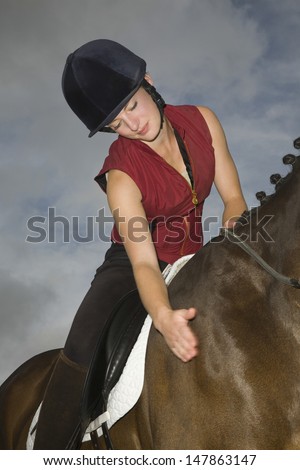 Low angle view of a female horseback rider stroking a cropped horse