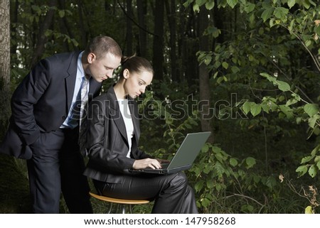 Side view of a business couple using laptop in the forest