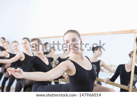 Row of female ballet dancers practicing at barre in rehearsal room