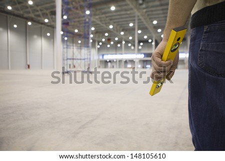 Midsection of manual worker holding spirit level in empty warehouse