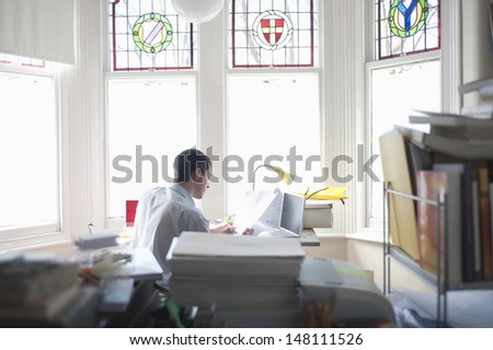 Rear view of businessman reading document in home office