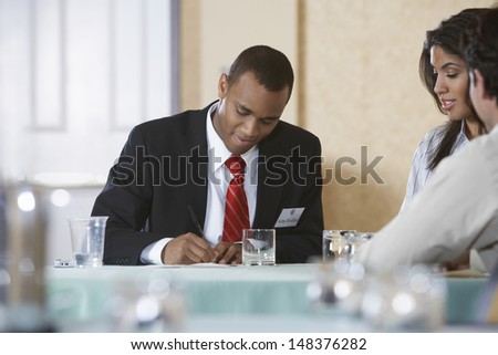 Businessman writing on document with coworkers sitting at desk in office