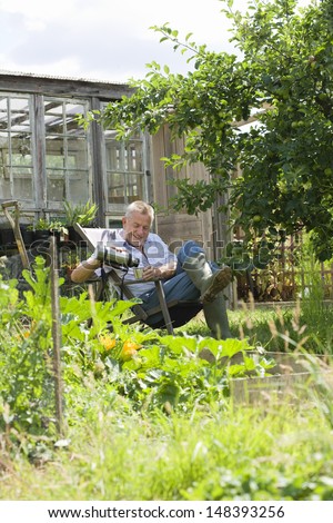 Happy senior man pouring drink while sitting in community garden
