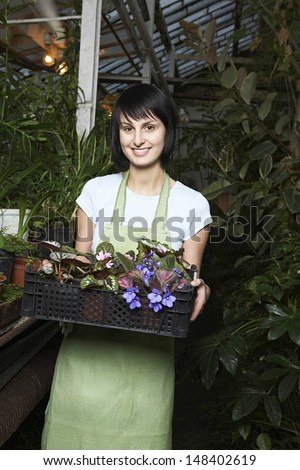 Portrait of young female botanist carrying crate full of flower plants at greenhouse