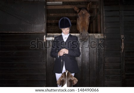 Young female horseback rider with horse and dog in the stable