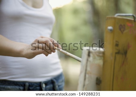 Midsection of young woman painting on canvas in park