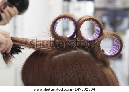 Female hairdresser rolling up curlers for her client in salon