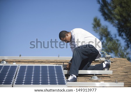 Full length side view of an African American man fixing solar panel on rooftop
