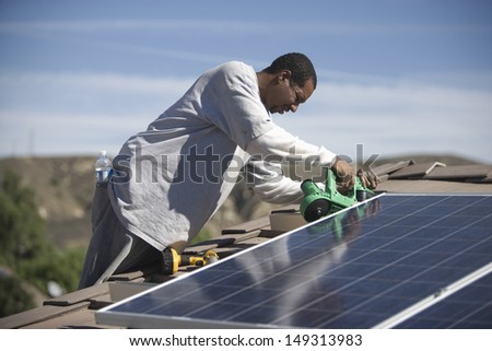An African American man working on solar panelling on rooftop