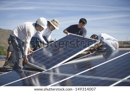 Group of multiethnic engineers placing solar panels on rooftop