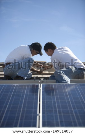 Two engineers working on solar panelling at rooftop against blue sky