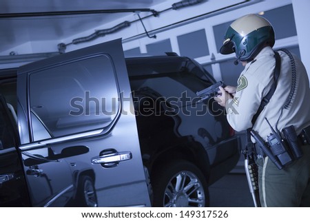 Rear view of middle aged traffic cop aiming handgun at car in garage