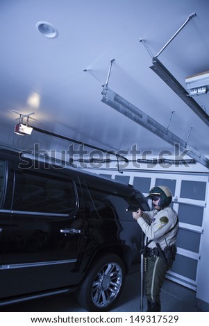 Side view of middle aged traffic cop aiming revolver while standing by car in garage