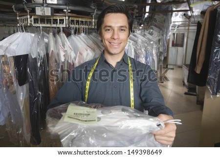 Portrait of confident young owner giving dry cleaned clothes in laundry