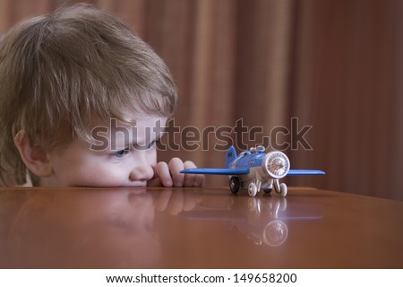 Little boy looking at toy airplane on table at home