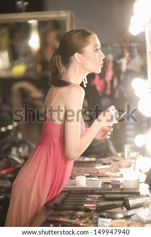 Side view of a female fashion model in pink slip looking at dressing room mirror
