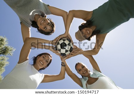 Directly below shot of female friends holding soccer ball against blue sky