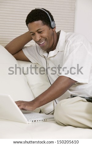 Happy man wearing headphones listening to music on laptop at home