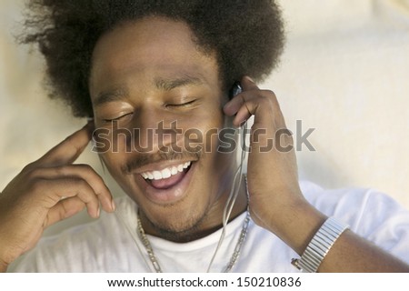 Closeup of happy young man with eyes closed enjoying music through earphones