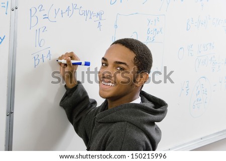 Portrait of smiling male student solving algebra equation on whiteboard in classroom