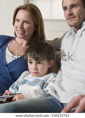 Cute little boy with father and mother watching television at home