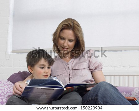 Loving mother and son reading book together on bed at home