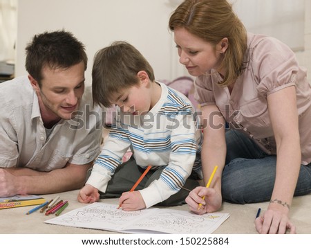 Young parents looking at son coloring in drawing book on floor