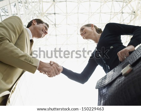 Low angle view of happy businessman and businesswoman shaking hands against ceiling