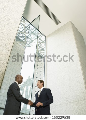 Low angle view of happy multiethnic businessmen shaking hands in office building