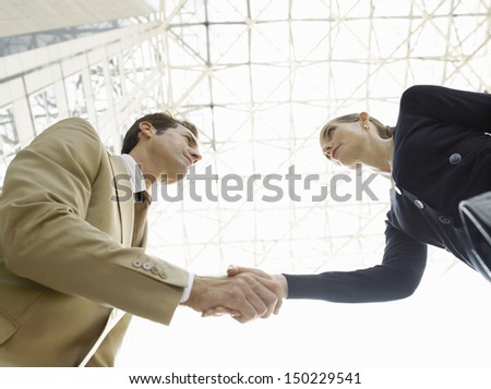 Low angle view of confident businessman and businesswoman shaking hands against ceiling