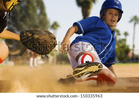 Full length of softball player sliding into home plate