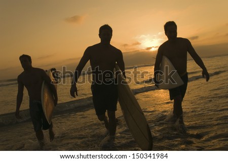 Full length of three surfers carrying surfboards out of surf at sunset