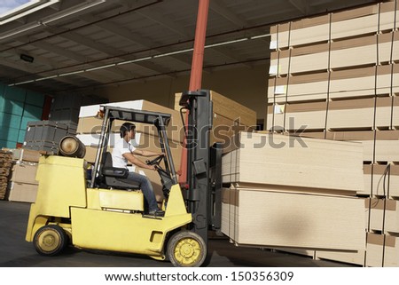 Side view of manual worker operating a forklift truck in lumber industry