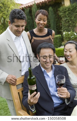 Middle aged man holding wine bottle and glass with friends in park