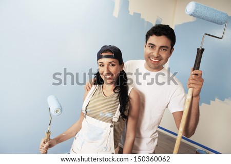 Portrait of smiling couple with paint rollers standing against partially painted wall